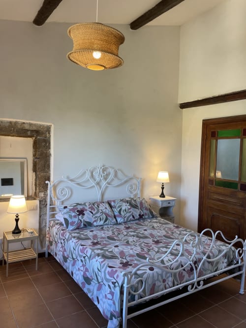 Camera elegante al Mater Familias Oasis B&B di Siracusa con letto in ferro battuto bianco ornamentale, biancheria floreale, lampada sospesa intrecciata, e