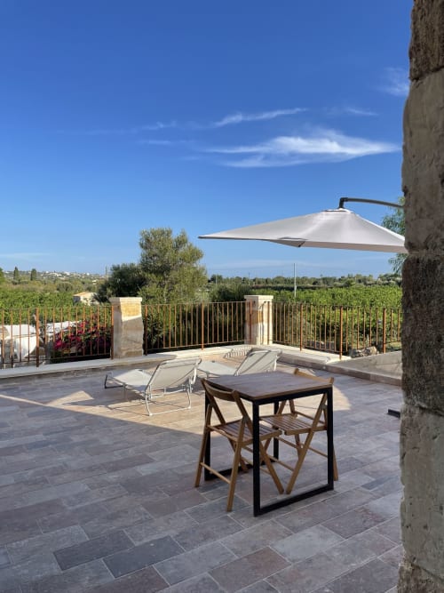 Terrazza di Mater Familias Oasis a Siracusa con tavolo, sdraio, ombrellone e vista sul giardino dei vigneti