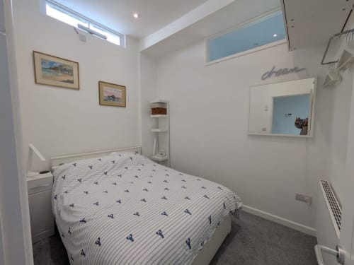 Bright bedroom at 2 Doves Holiday Property in Exeter with white walls, single bed, mirror, and coastal artwork