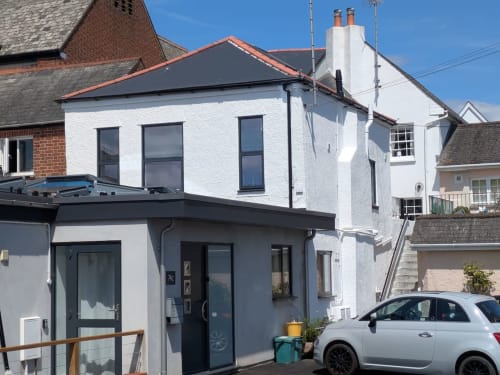 2 Doves Holiday Property in Exeter: Modern white holiday home with dark-trimmed extension, parked car, and blue roof.