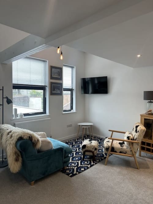 Modern loft bedroom at 2 Doves Holiday Property in Exeter with sloped ceiling, blue armchair, wooden chair, wall-mounted TV,