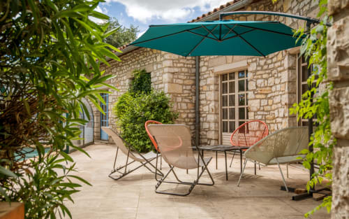Terrasse extérieure de la villa Casa de la huerta à Millau avec parasol cantilever turquoise, mobilier de détente, bâtisse en pierre et verdure luxuriante