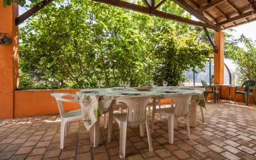 Terrasse ombragée de Casa de la huerta à Millau avec chaises et table blanches, entourée de verdure luxuriante