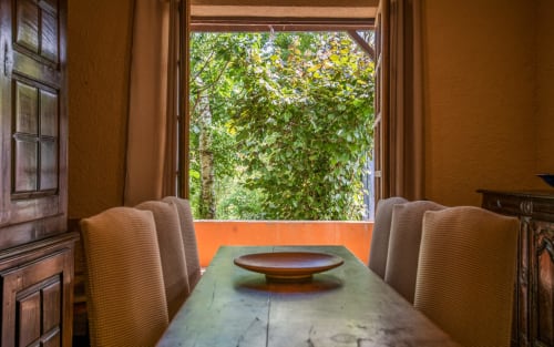 Salle à manger avec table en bois, chaises rembourrées et vue sur le jardin luxuriant de la villa Casa de la huerta à Millau