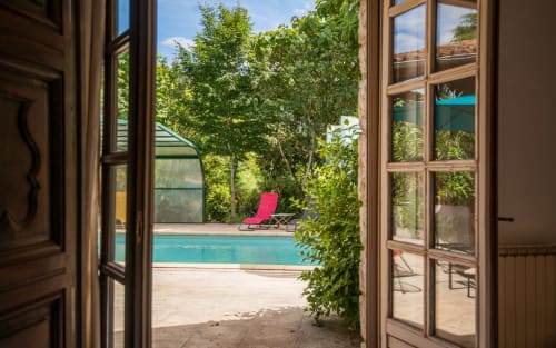 Vue à travers les portes ouvertes de la piscine privée de la villa Casa de la Huerta avec transat rose et jardin luxuriant à Millau, France
