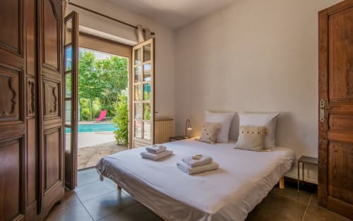 Chambre lumineuse avec portes-fenêtres vue piscine à la villa Casa de la huerta à Millau, lit blanc et mobilier en bois