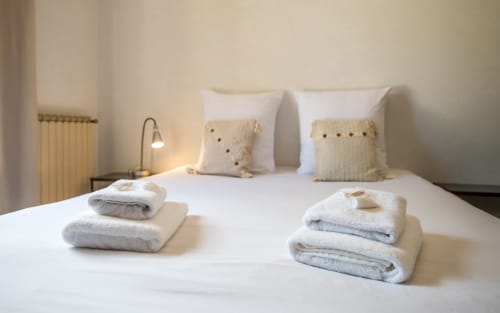 Chambre accueillante avec draps blancs, serviettes empilées, coussins décorés et lampe chaleureuse à la villa Casa de la huerta à Millau