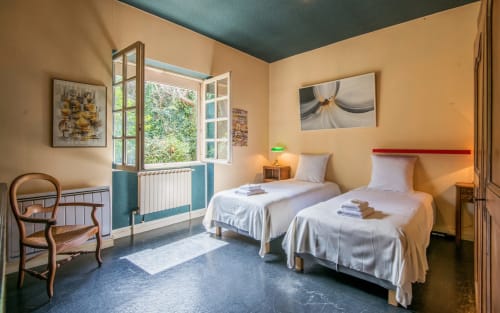 Chambre double lumineuse avec plafond bleu-vert, grandes fenêtres, murs jaune pâle et deux lits blancs aux draps frais à Casa de la