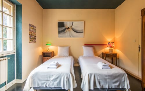 Deux lits jumeaux aux draps blancs dans une chambre jaune lumineux à la villa Casa de la huerta à Millau, France