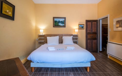 Chambre lumineuse avec lit bleu, tête de lit en bois, deux lampes et murs jaunes à la villa Casa de la huerta à Millau