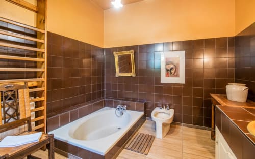 Salle de bains spacieuse de la villa Casa de la huerta à Millau avec carrelage marron, baignoire blanche, lavabo sur pied et parquet