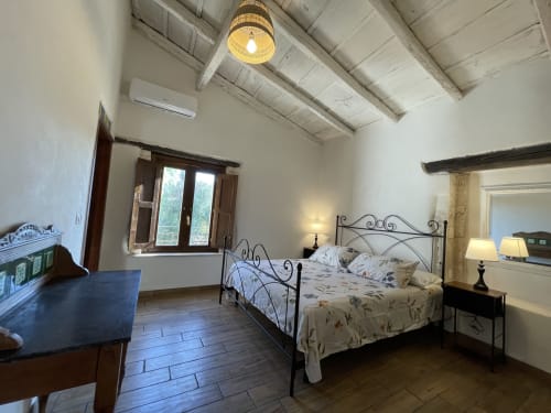 Spacious bedroom with wrought iron bed, wooden beams, and garden view at Mater Familias Oasis, Siracusa