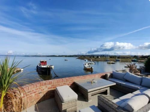 Waterfront terrace at 2 Doves Holiday Property with moored boats, sea views, and comfortable outdoor seating near Exeter