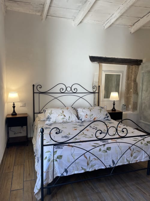 Camera elegante presso Mater Familias Oasis Siracusa con letto in ferro battuto, biancheria floreale e vista sul giardino