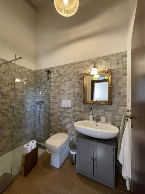 Bagno moderno presso Mater Familias Oasis a Siracusa con pareti in mattoni grigi, lavandino bianco, WC e doccia in vetro