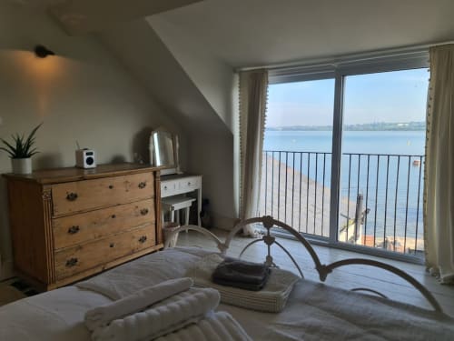 Bright Exeter beachfront bedroom with panoramic sea views, wooden furniture, and private balcony overlooking bay.