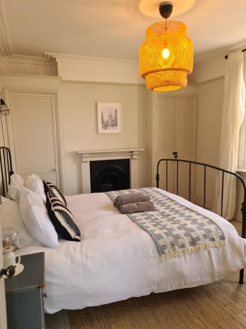 Elegant bedroom at 2 Doves Holiday Property in Exeter with metal bed frame, white linens, woven pendant light, and fireplace.