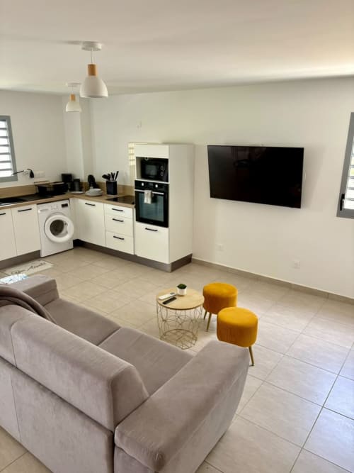 Séjour ouvert et moderne à Maly Blue Location avec canapé crème, cuisine, TV écran plat et tabourets jaunes au Havre