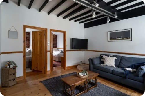 2 Doves Holiday Property living area with dark sofa, wooden beams, and doors to bedrooms in Exeter