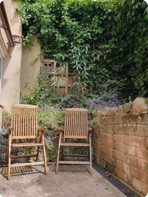Two wooden chairs in lush courtyard garden at 2 Doves Holiday Property, Exeter