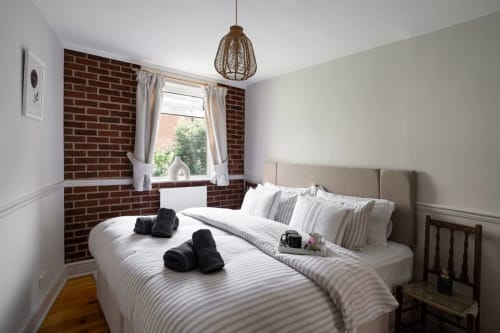 Modern bedroom at 2 Doves Holiday Property, Exeter with exposed brick, beige upholstered headboard and pendant lighting