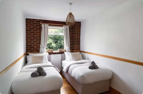 Twin bedroom at 2 Doves Holiday Property in Exeter with white bedding, rolled towels, brick wall, and large window with