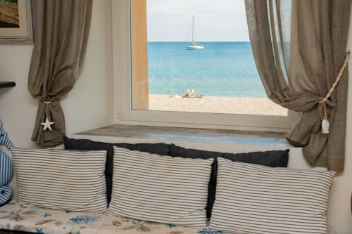 Accogliente vista dalla finestra della camera da letto sulla spiaggia di Varigotti con barca a vela, cuscini rigati e tende vista mare dell'appartamento Ancora