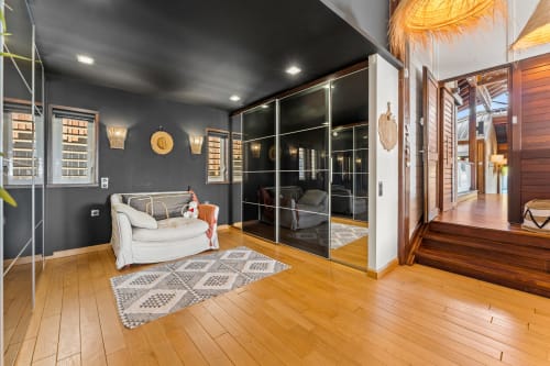 Chambre de villa moderne aux murs sombres, fauteuil blanc, placard miroir, sol en bois aux Balcons D'Oyster Pond