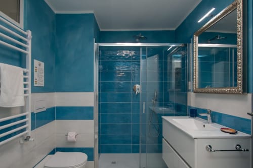 Bagno moderno con piastrelle azzurre, doccia walk-in, lavabo e specchio bianco nell'appartamento con vista mare di Welcome Varigotti