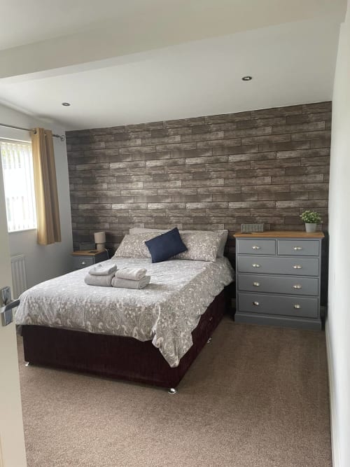 Modern bedroom at 2 Doves Holiday Property, Exeter with wooden feature wall, double bed, grey dresser and natural light