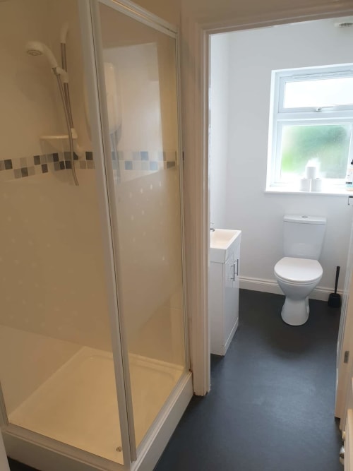 Modern bathroom at 2 Doves Holiday Property in Exeter with shower enclosure, white toilet, sink, and dark tile flooring