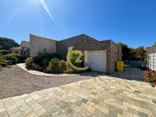 Villa moderne à L'Île-Rousse avec façade en pierre, porte de garage blanche, allée pavée et jardins méditerranéens