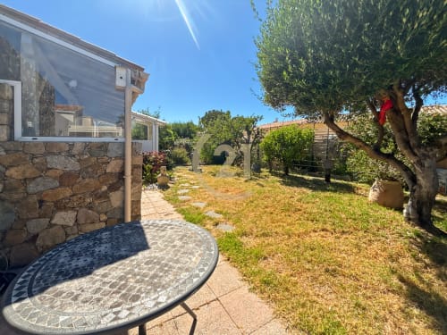 Terrasse ensoleillée de la villa Marine de Sant Ambroggio à L'Île-Rousse avec murs en pierre, olivier et table de patio