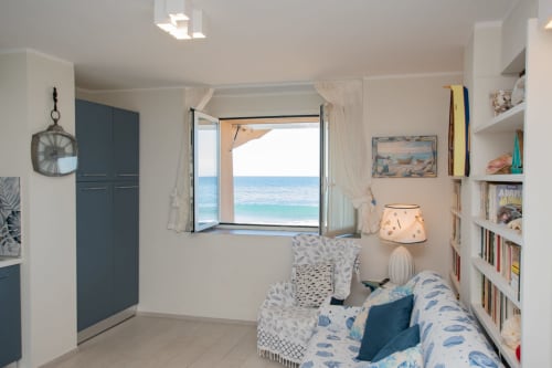 Camera da letto luminosa con vista mare, scaffali bianchi, accenti blu e arredamento costiero a Welcome Varigotti