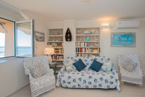 Soggiorno con vista mare in appartamento costiero, divano bianco-blu a tema marino, scaffali e arredamento marinaro a Welcome Varigotti