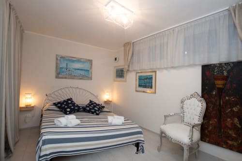 Camera Faro al Welcome Varigotti di Finale Ligure con letto rigato, poltrona elegante e opere d'arte costiera
