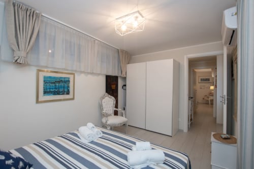 Spaziosa camera d'albergo al Welcome Varigotti con letto a righe, guardaroba, poltrona e finestra con vista mare