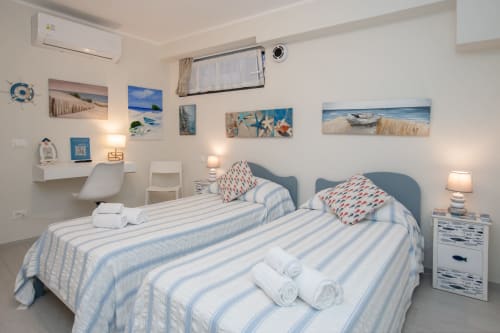 Camera luminosa al Welcome Varigotti con due letti, arredamento a tema marino, opere d'arte costiera e comfort moderni a Finale Ligure