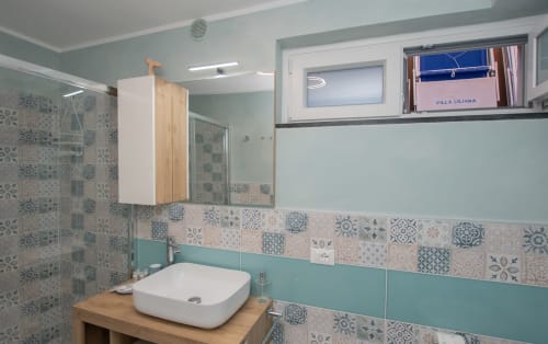 Bagno moderno dell'hotel Welcome Varigotti a Varigotti con piastrelle a motivi, lavabo bianco, pareti turchesi e doccia
