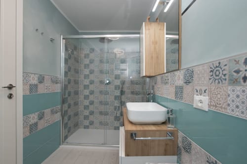Moderno bagno con piastrelle turchesi e decorate, mobile in legno, lavabo bianco rotondo all'hotel Welcome Varigotti