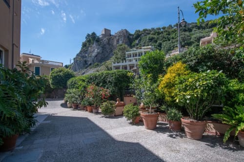 Terrazza di Varigotti con vasi di fiori, vista mare verso le rovine del castello, atmosfera mediterranea