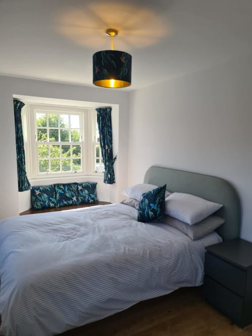 Modern bedroom at 2 Doves Holiday Property in Exeter with grey upholstered bed, patterned cushions, and large bay window