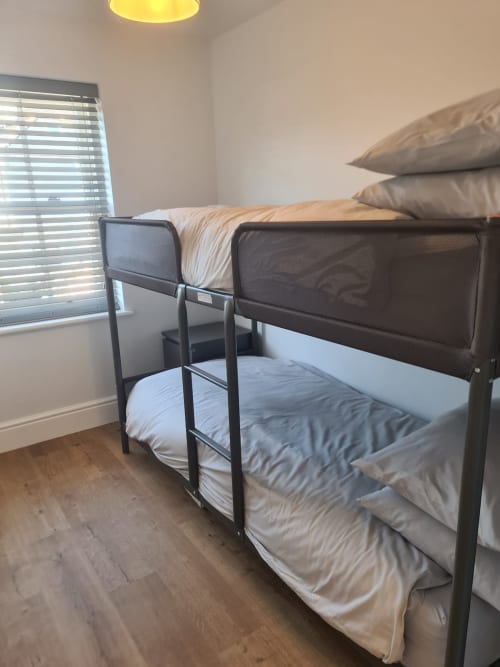 Bunk bed room at 2 Doves Holiday Property in Exeter with dark metal frame, white bedding, and window with blinds