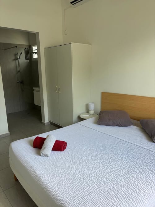 Chambre moderne à Maly Blue Location au Moule : lit queen-size, literie blanche, serviettes rouges, armoire et salle de bain attenante