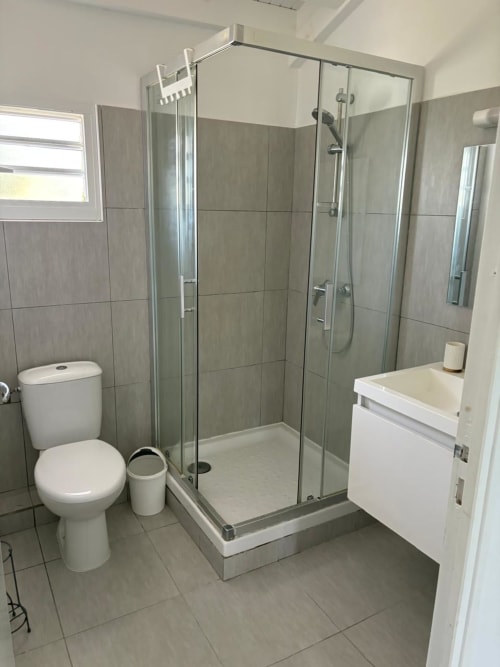 Salle de bain moderne à Maly Blue Location au Moule avec douche vitrée, vasque blanche et toilettes