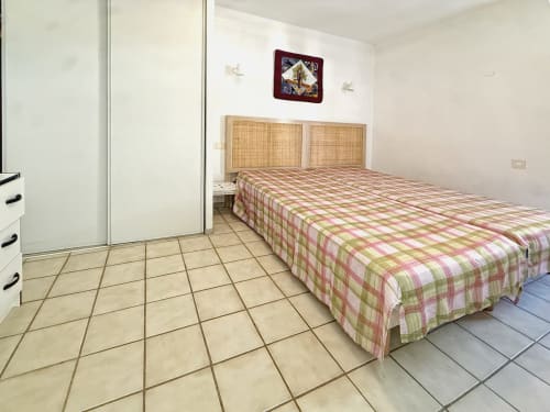 Chambre spacieuse avec couvre-lit à carreaux, tête de lit en rotin, armoire et carrelage à l'hôtel LOCADIGNE