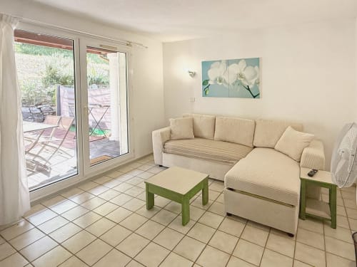Séjour lumineux avec canapé sectionnel crème, tables vertes et accès à la terrasse à LOCADIGNE Digne-les-Bains