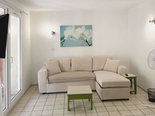 Lumineux salon d'appartement LOCADIGNE avec canapé sectionnel crème, tableau orchidée blanc, table d'appoint verte et carrelage