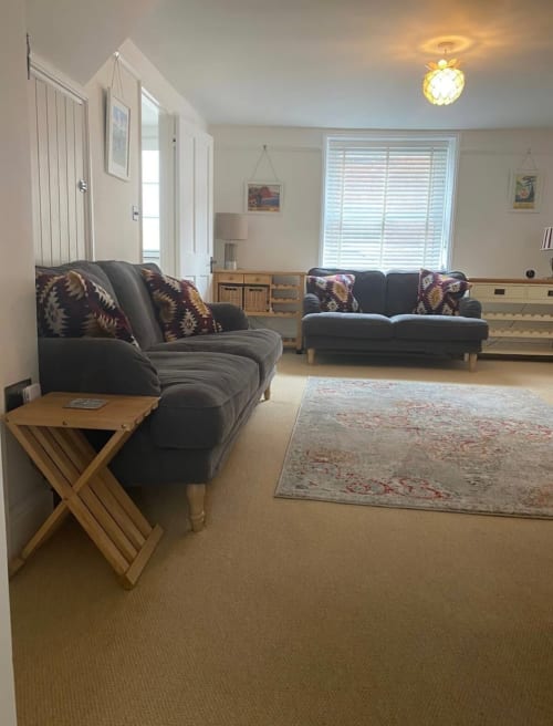 Spacious living room at 2 Doves Holiday Property in Exeter with two charcoal sofas, wooden side table, and cream carpeting.