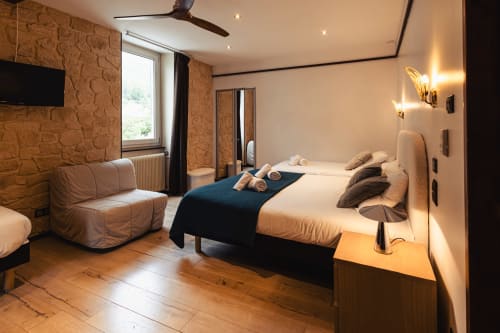 Chambre familiale moderne à l'Hôtel Savoy avec mur en pierre, lit, coin salon et vue sur les montagnes au Bourget-du-Lac